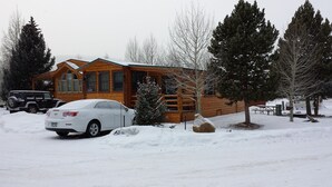 A wooden cabin with a covered porch, a car parked in front, and snow on the ground.