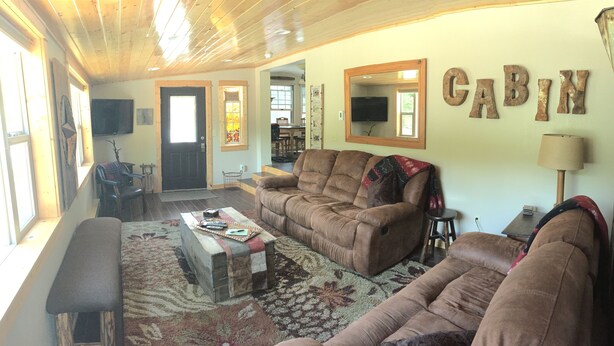 A cozy cabin interior with two sofas, a bench, a coffee table, and a TV.