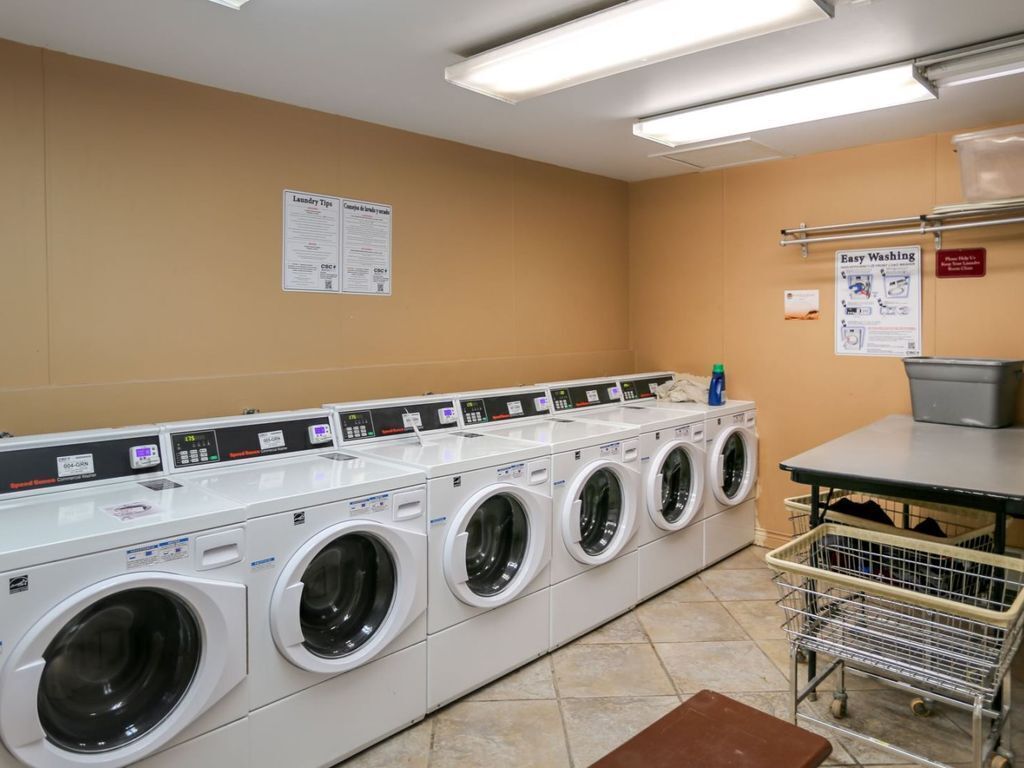 A laundry facility with multiple washing machines, a metal cart, and informational posters on the walls.