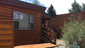 A wooden cabin with a covered outdoor seating area and a staircase leading to an upper level.
