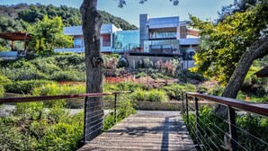 A modern building with a glass facade, surrounded by lush greenery and a wooden pathway leading to it. - Private Custom Modern 10,000 sq. Ft. Estate -- Nestled on 15 Acres (Temecula)