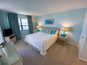 A bedroom with a bed, two bedside tables with lamps, a television on a stand, a window with curtains, and a picture on the wall. - Sanibel Harbour Resort Bay View Tower 433:   Renovated condo with gorgeous sunset views (Fort Myers)