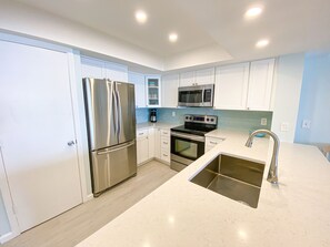A modern kitchen with stainless steel appliances, white cabinetry, and a large sink.