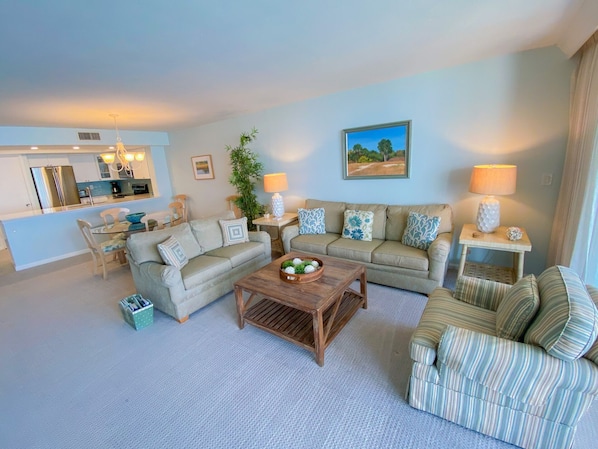 A living room with a sofa, armchair, and coffee table, a dining area with chairs and a table, and a kitchen with a refrigerator and stove. - Sanibel Harbour Resort Bay View Tower 433:   Renovated condo with gorgeous sunset views (Fort Myers)