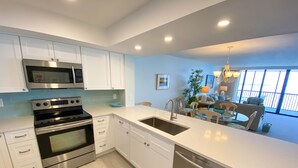 A modern kitchen with stainless steel appliances, white cabinetry, and a large window providing a view of the outdoors. - Sanibel Harbour Resort Bay View Tower 433:   Renovated condo with gorgeous sunset views (Fort Myers)