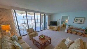 A spacious living room with a large sofa set, a coffee table with decorative items, a television, and a view of the sea through large windows. - Sanibel Harbour Resort Bay View Tower 433:   Renovated condo with gorgeous sunset views (Fort Myers)