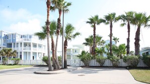 A beachfront hotel with multiple-story buildings, palm trees, and a white picket fence. - Quiet, Big, Bright and Beautiful!  Perfect Beach House for Family and Friends (Port Aransas)