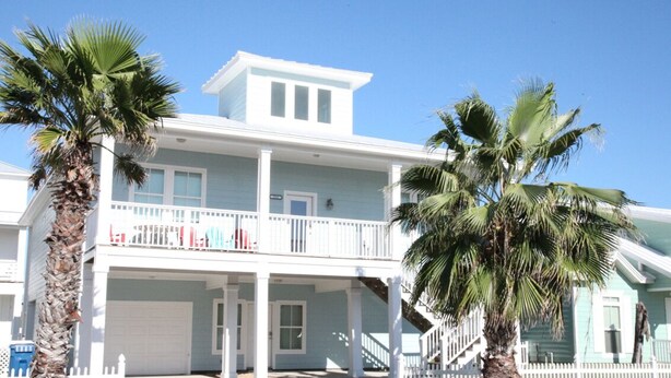 A two-story house with a balcony, a garage, and palm trees. - Quiet, Big, Bright and Beautiful!  Perfect Beach House for Family and Friends (Port Aransas)