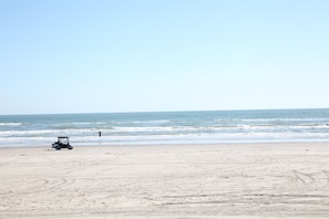Ein Strand mit einem Golfwagen im Sand und dem Meer im Hintergrund.