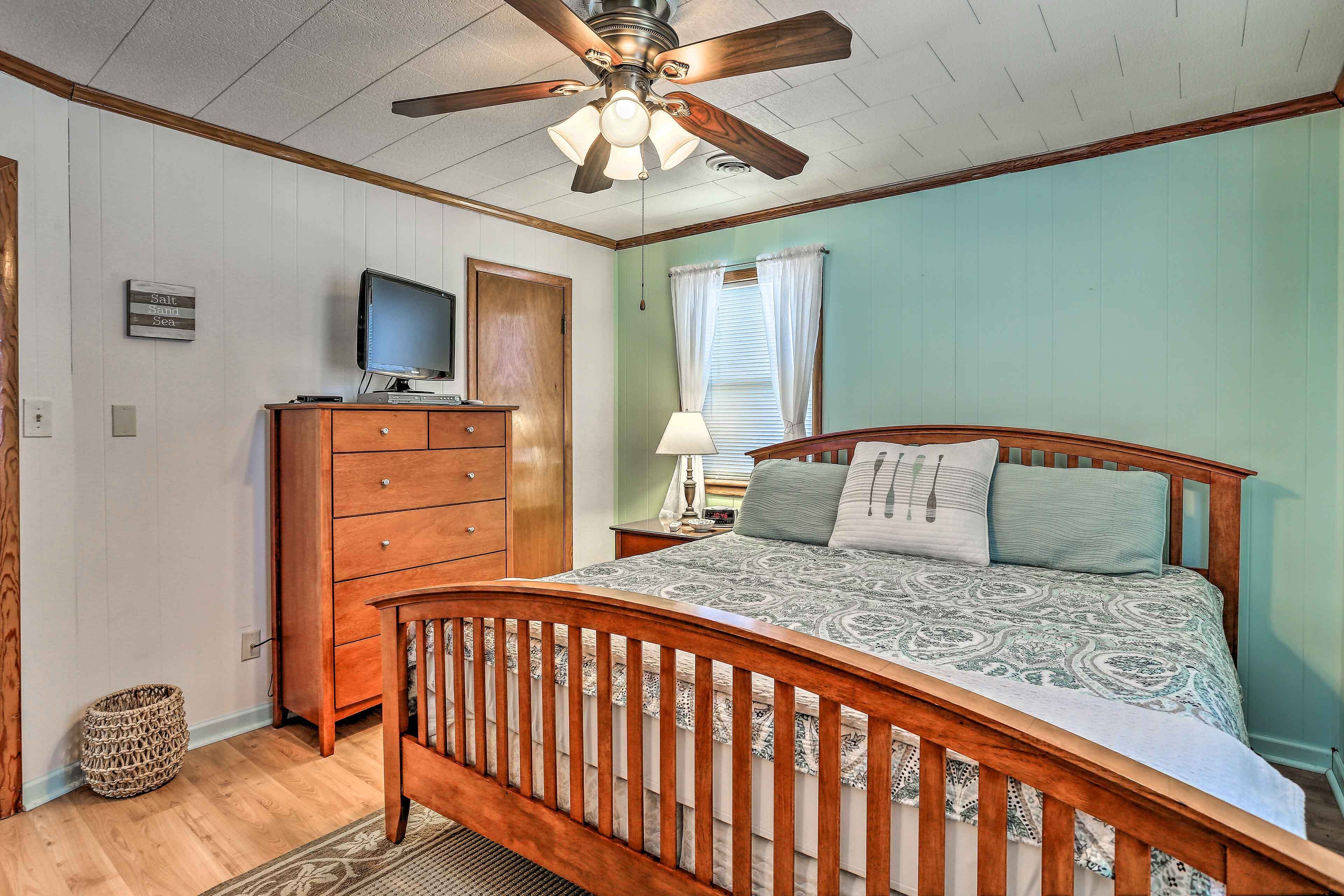 A bedroom with a wooden bed, a ceiling fan, a television on a dresser, and a window with curtains.