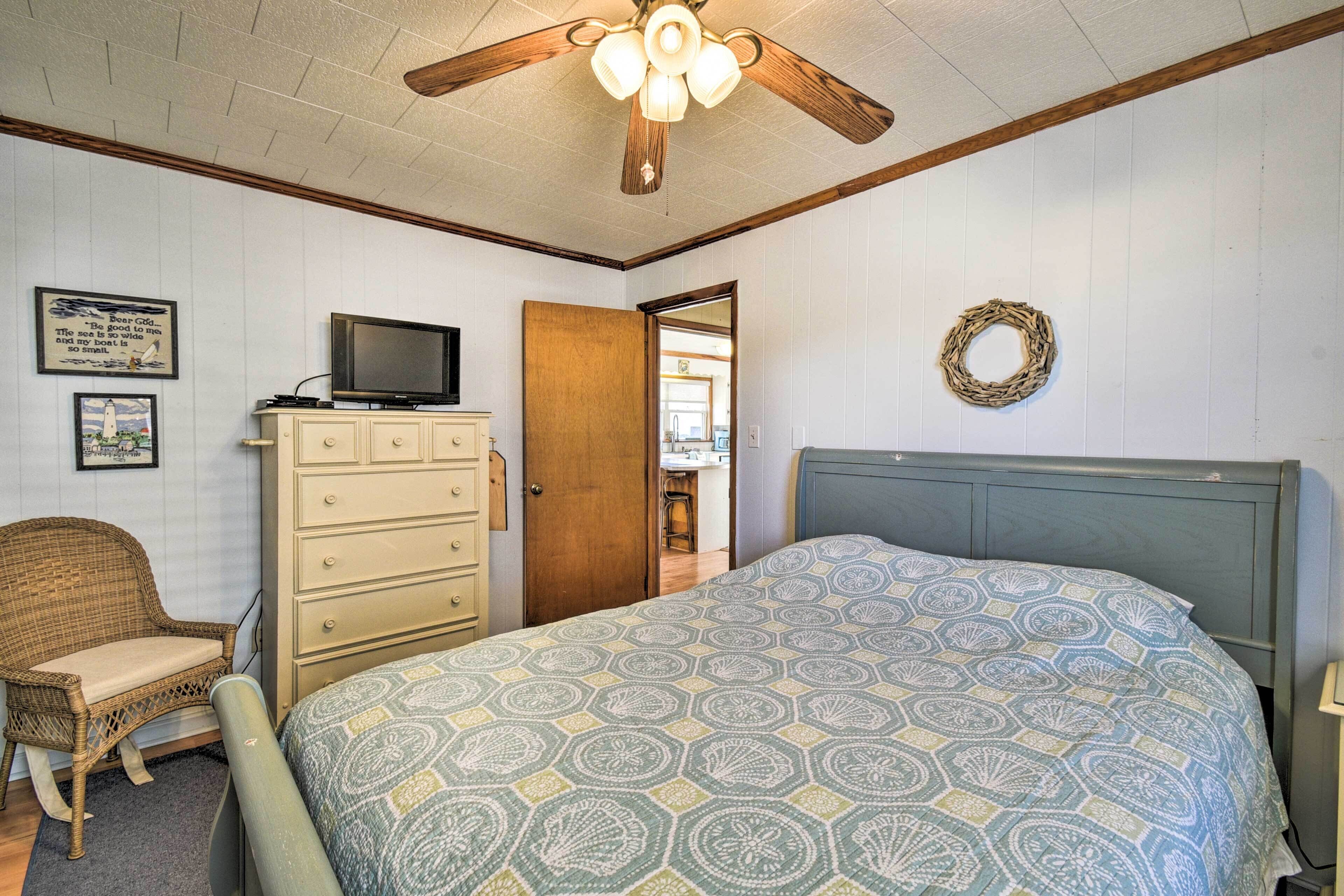 Un dormitorio con cama, cómoda, televisor y ventilador de techo.