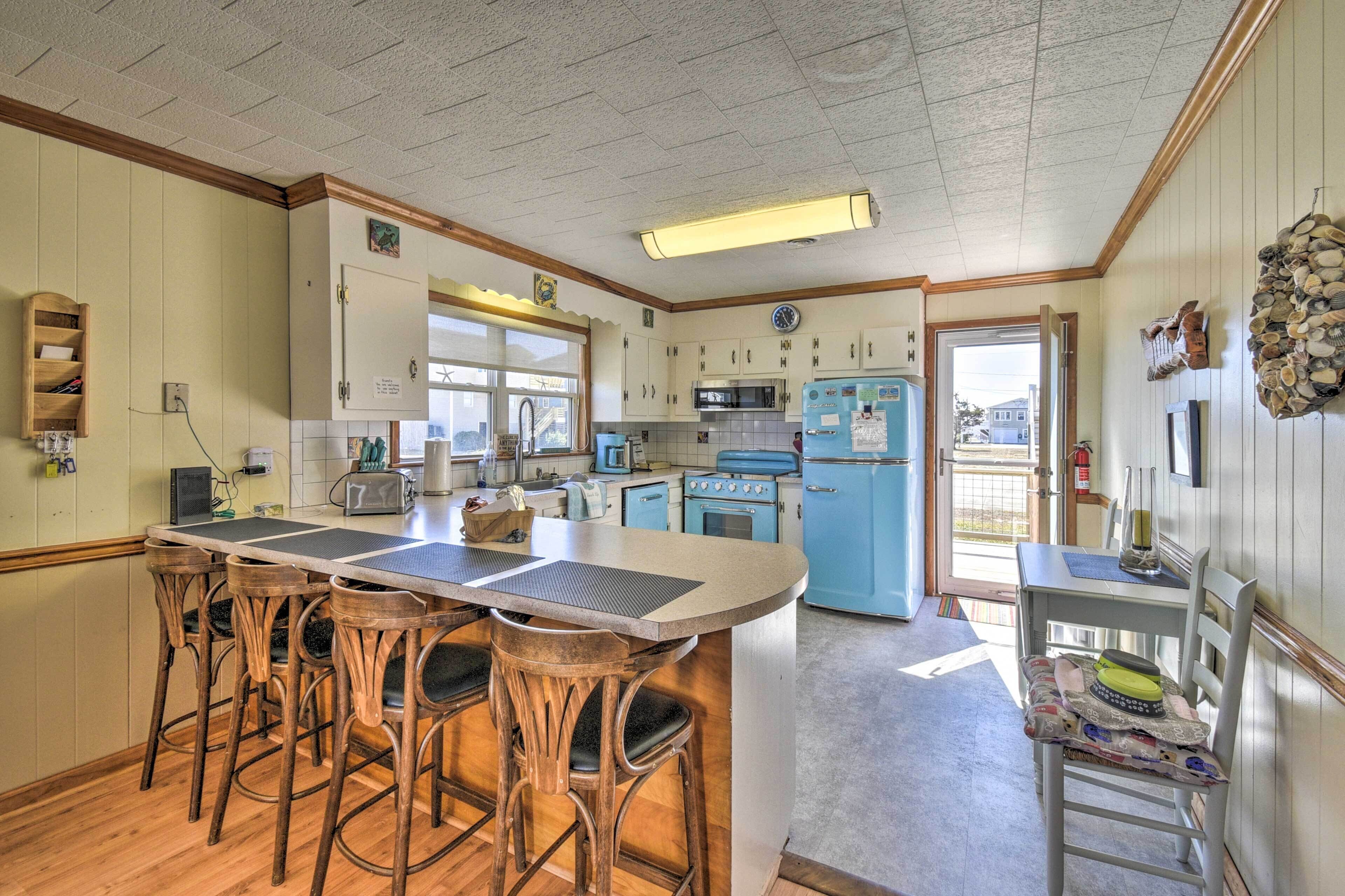A kitchen with a central island, bar stools, wooden chairs, a microwave, a stove, and a refrigerator.