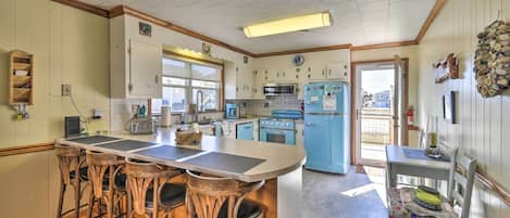 A kitchen with a central island, bar stools, wooden chairs, a microwave, a stove, and a refrigerator.