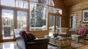 A log cabin interior with a leather sofa, a wooden coffee table, and a view of snow-capped mountains through large windows. - 5 BR + Loft Luxury Ski-in & Ski-out Log Home, stunning mountain views, hot tub (Mt Village)