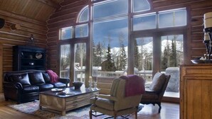 A log cabin interior with a large window offering a view of snow-capped mountains and trees. - 5 BR + Loft Luxury Ski-in & Ski-out Log Home, stunning mountain views, hot tub (Mt Village)