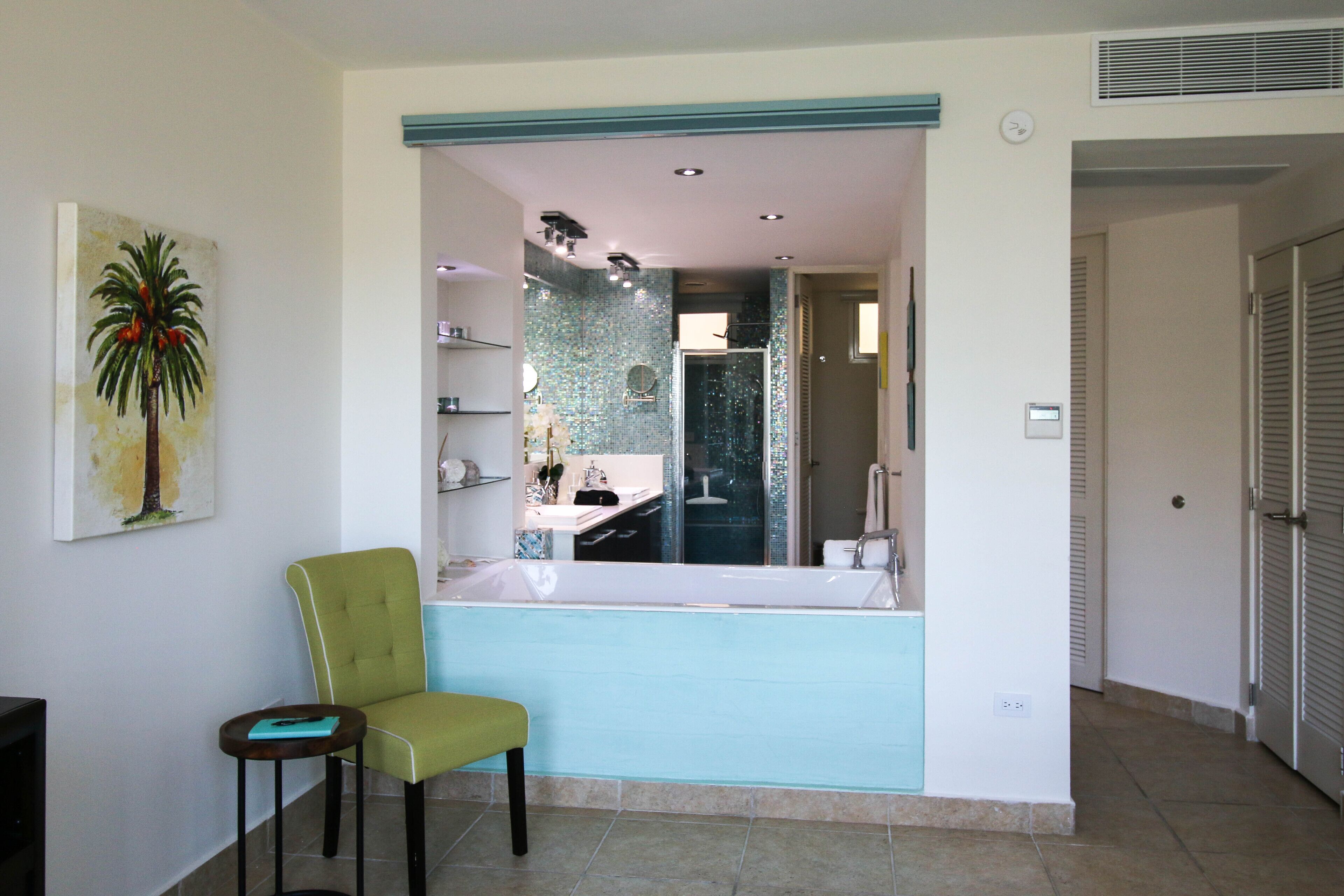 A bathroom with a large mirror, a green chair, and a sink.