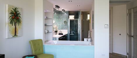 A bathroom with a large mirror, a green chair, and a sink.