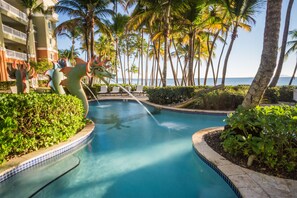 A swimming pool with a decorative sea creature sculpture, surrounded by palm trees and a hotel building.