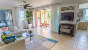 A modern living room with a sofa, coffee table, and TV. There is a balcony with a chair and a potted plant.
