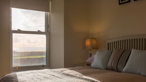 A bedroom with a large window, a bed with a striped headboard, and a bedside lamp. - Castle View House, stunning period property. (Doolin)