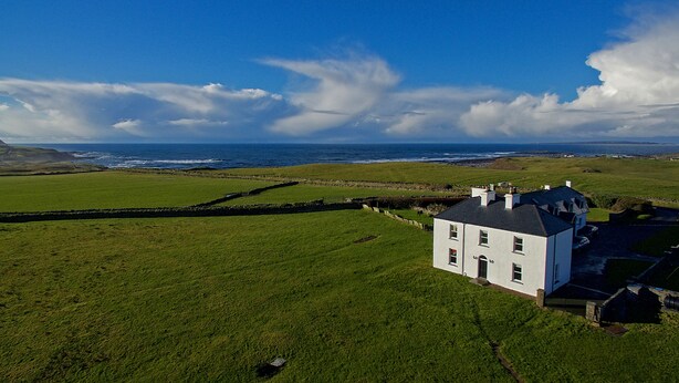 A white house with a stone wall and a view of the ocean. - Castle View House, stunning period property. (Doolin)