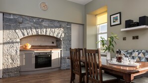 A kitchen with a stone wall, wooden cabinets, and a built-in oven. There is a dining table with chairs and a tray with a teapot and cups. - Castle View House, stunning period property. (Doolin)