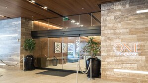 En modern hotellentrés med en glasdörr, krukväxter och en skylt med texten ”ONE ALA MOANA”.