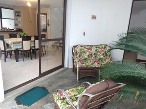 Una zona de menjador amb taula i cadires, un sofà de vimetlla i una planta gran en test.