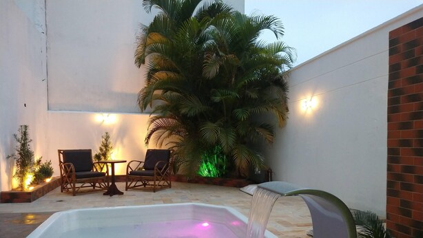 A pool area with a water feature, two wicker chairs, and a large palm tree.