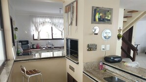 A compact kitchen with a sink, a bar stool, and a small trash bin.