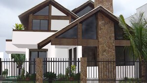A modern two-story house with a stone facade, large windows, and a black metal fence.