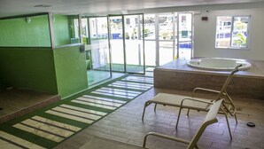 A room with a green wall, a wooden floor, a striped rug, and a window with a view of buildings outside. - Beachfront apartment in Praia do Futuro with full amenities. (Antonio Diogo)