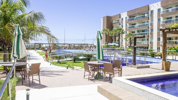 A hotel pool area with outdoor seating, palm trees, and a building with multiple balconies. - Beachfront apartment in Praia do Futuro with full amenities. (Antonio Diogo)