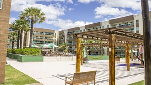 A courtyard with a wooden pergola, palm trees, and outdoor seating. - Beachfront apartment in Praia do Futuro with full amenities. (Antonio Diogo)