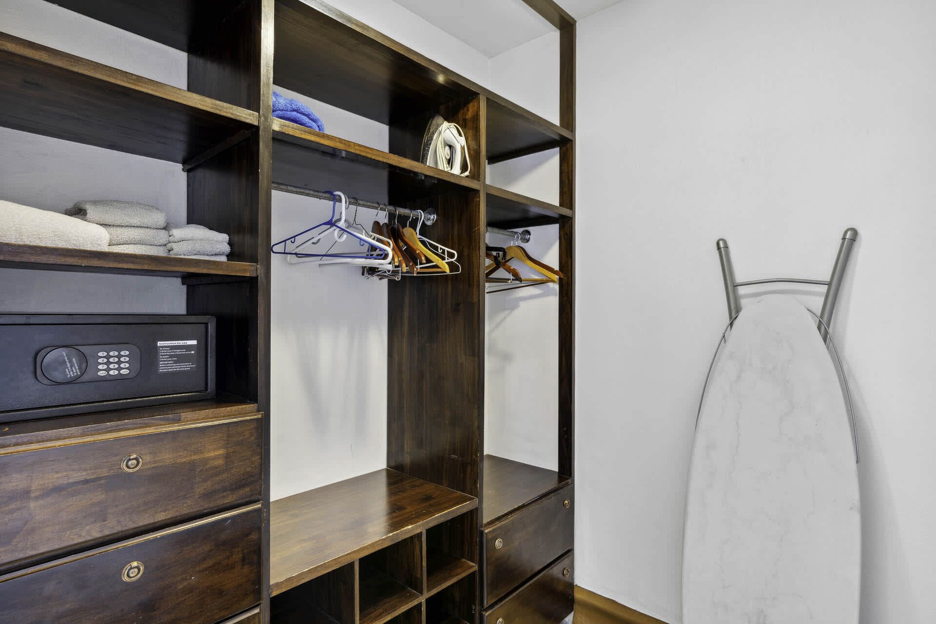 Un dressing avec des étagères en bois, une tringle à vêtements et une planche à repasser escamotable.