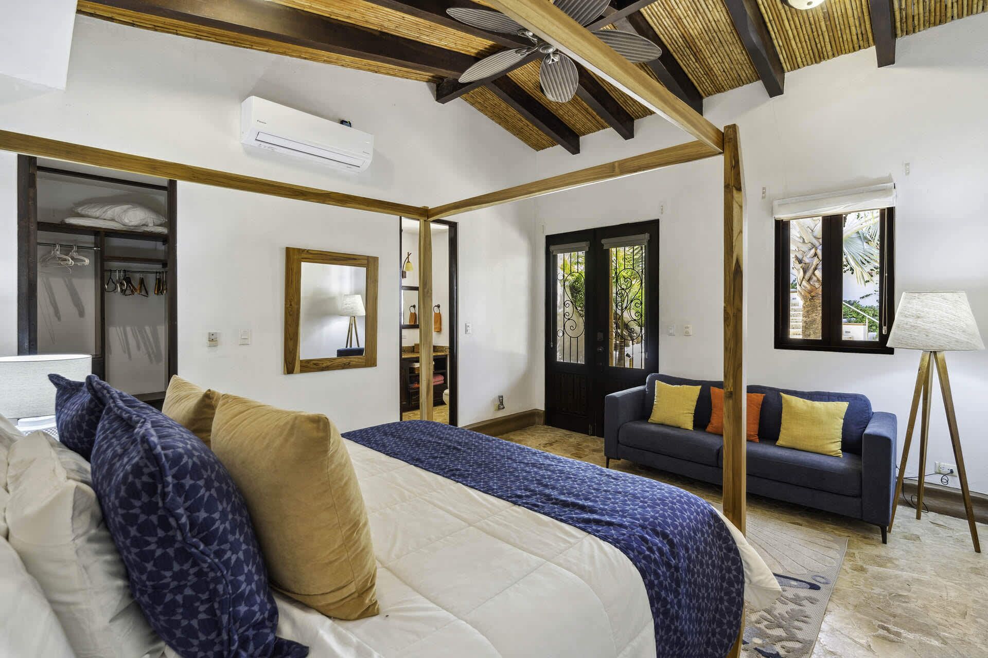 A bedroom with a bed, a sofa, a standing lamp, and a window with a view.