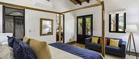 A bedroom with a bed, a sofa, a standing lamp, and a window with a view.