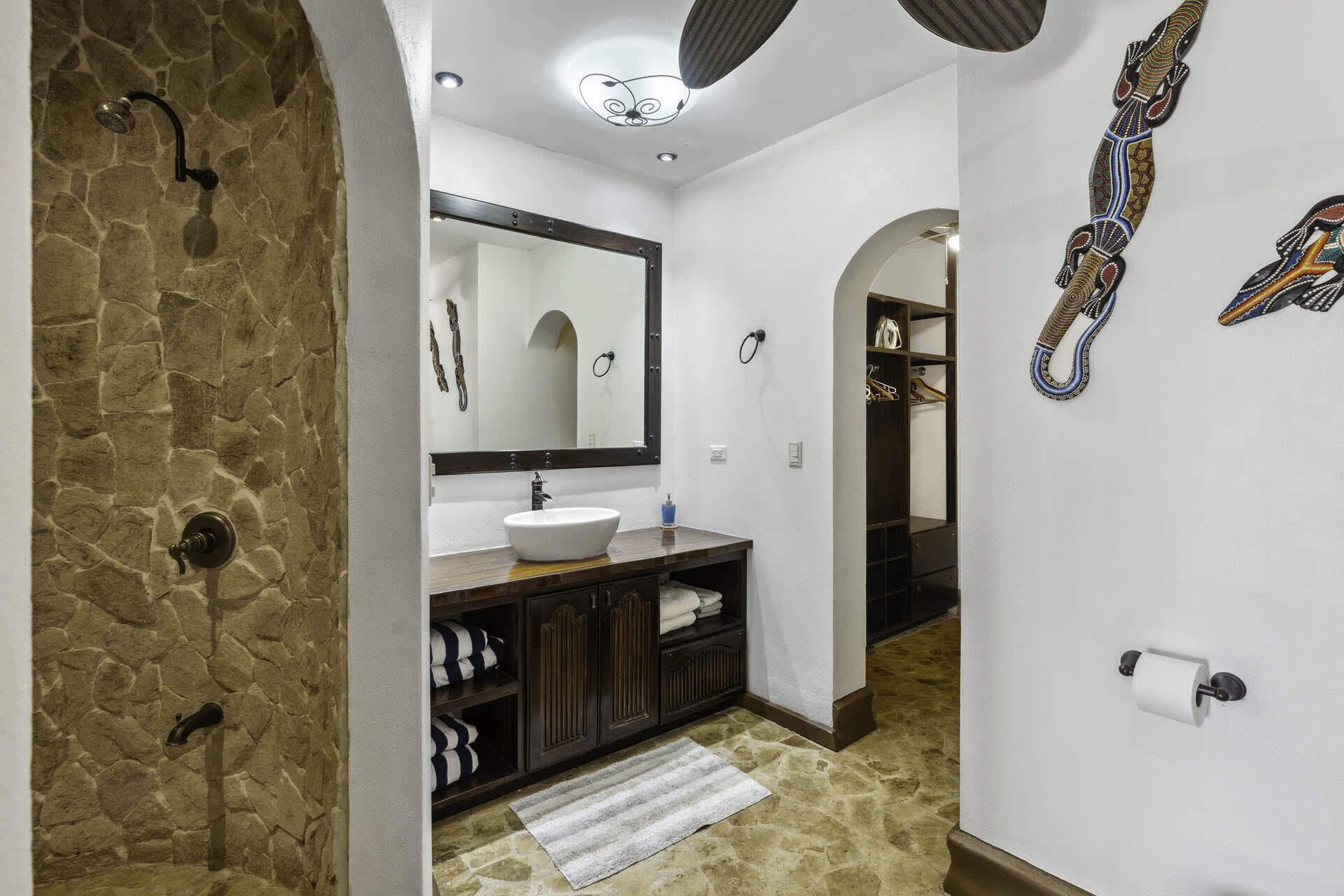 Un baño con pared de piedra, un lavabo blanco, un espejo, un perchero para toallas y una ducha.