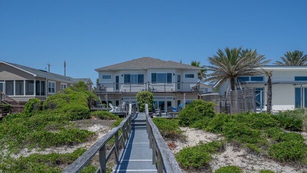 Una proprietà fronte spiaggia con una passerella in legno che conduce a una casa a due piani con un balcone.