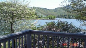 Blick von einem Balkon auf einen See mit umliegender Natur und Hügeln.