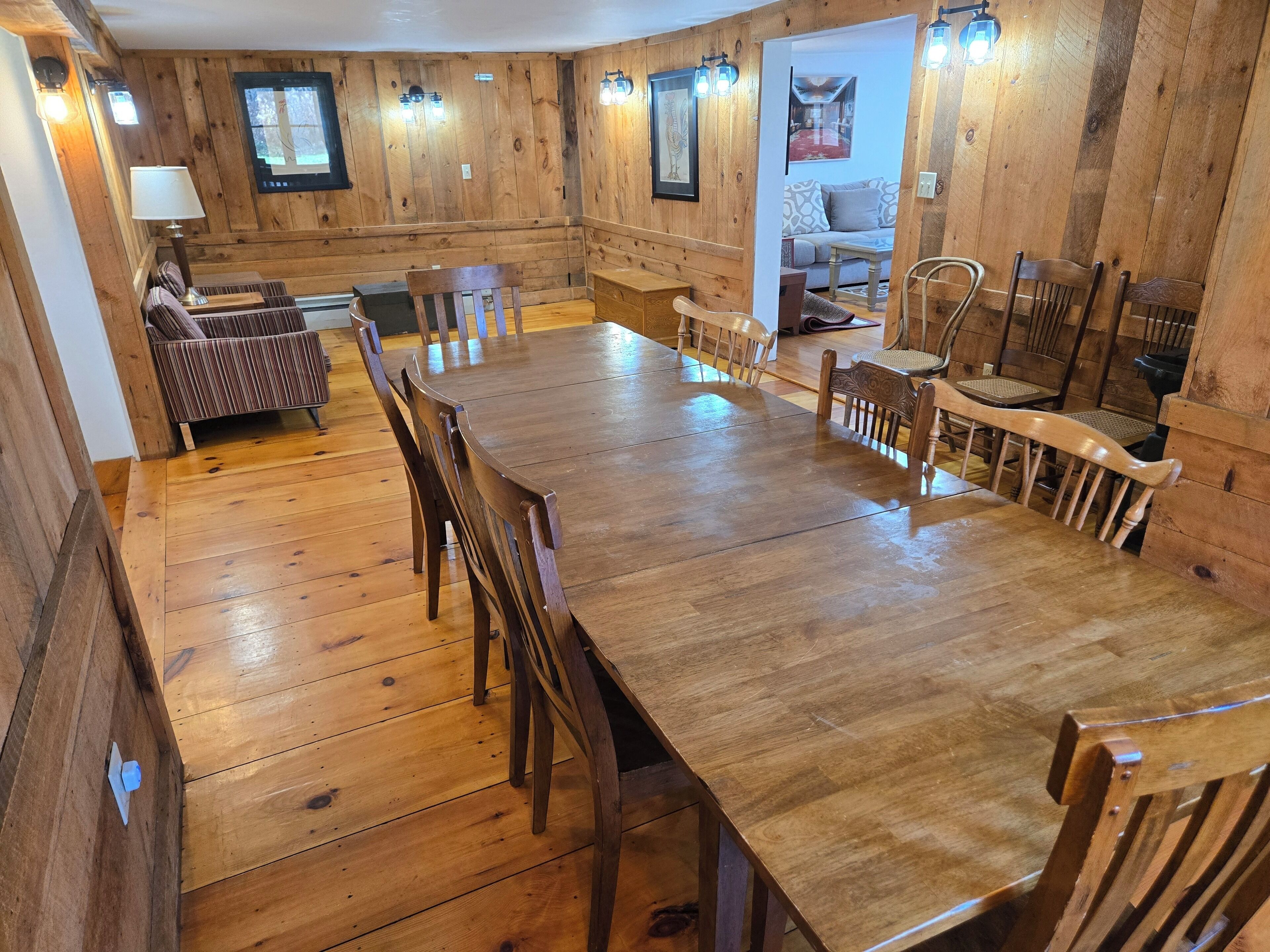 Ein geräumiger Essbereich aus Holz mit einem langen Tisch und mehreren Stühlen, umgeben von Holzwänden und einer gemütlichen Sitzecke mit einer Couch und Sesseln.