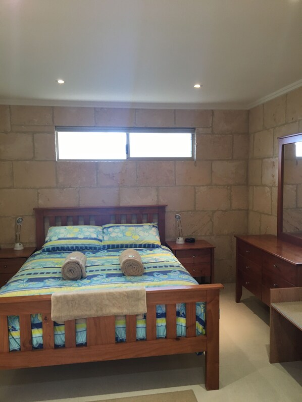 A bedroom with a wooden bed, a nightstand, a dresser, and a window with a view.