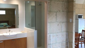 Une salle de bain moderne avec un grand lavabo, un miroir et une douche. On y trouve également un porte-serviettes et un petit tapis sur le sol.