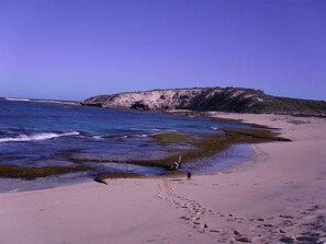 A beach with clear blue water, a sandy shore, and rocky cliffs in the background.