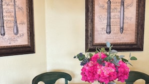 Una mesa de vidrio redonda con un florero transparente de flores rosadas, rodeada de sillas tapizadas en verde.
