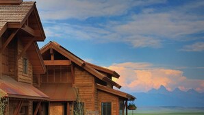 A large wooden house with a stone foundation, a porch, and a view of mountains in the background. - Luxury home with Stunning 4 Peak Views (Tetonia)