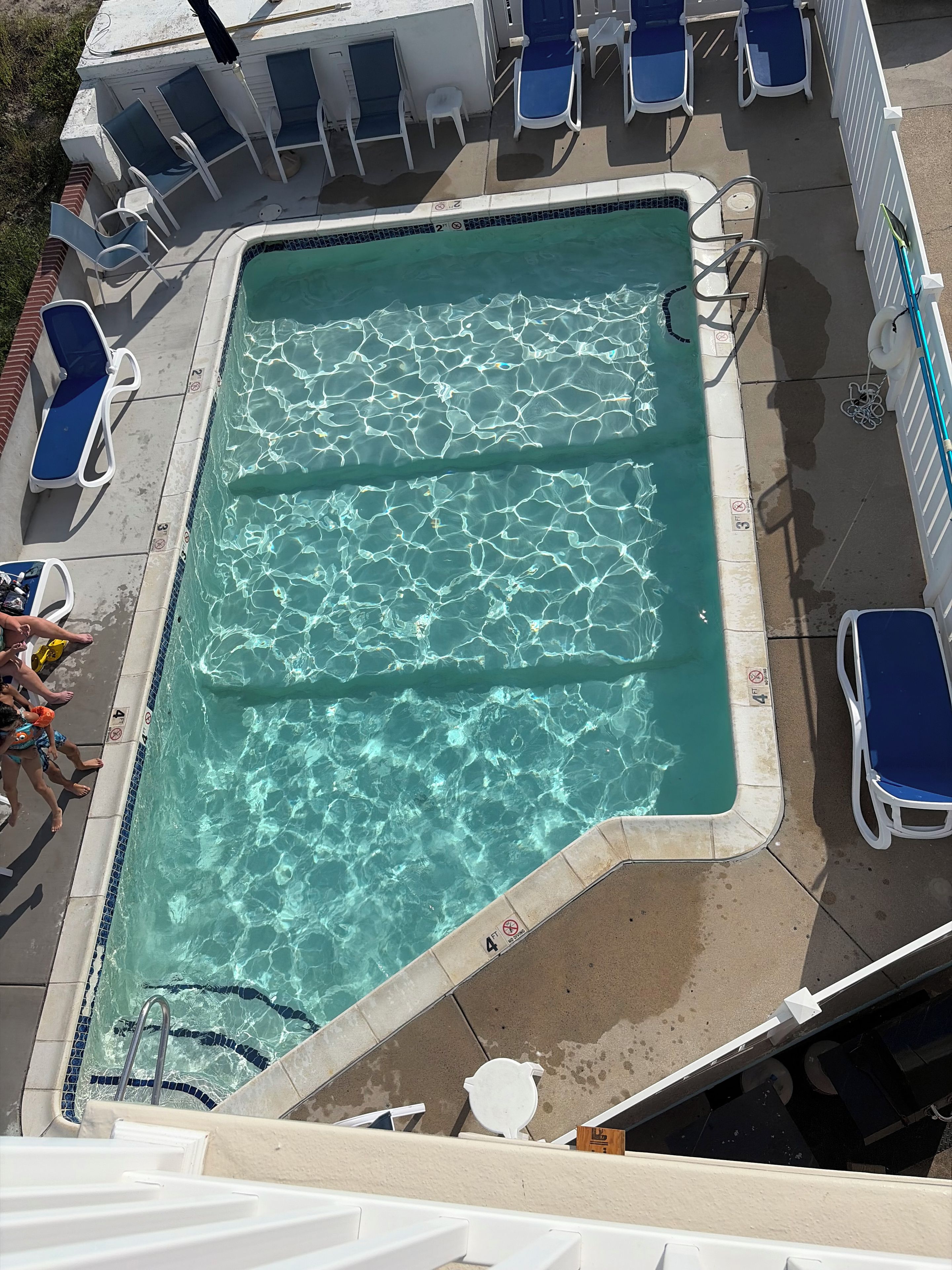 A rectangular pool with clear water, surrounded by white lounge chairs and a white fence.