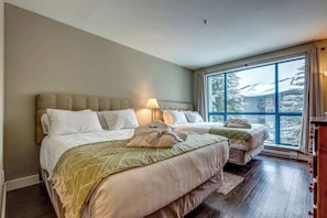 A hotel room with two beds, a large window, and a wooden floor.