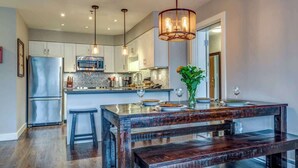 Une cuisine moderne dotée d’un îlot central, d’appareils électroménagers en acier inoxydable, de luminaires suspendus et d’un banc en bois.