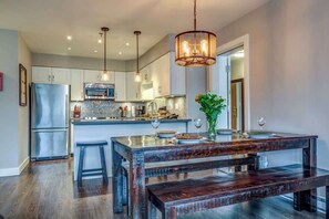 A modern kitchen with a central island, stainless steel appliances, pendant lighting, and a wooden bench. - Greystone Lodge 221 Ski-in/Out by Acer Vacations (Whistler)